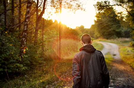 man wearing hoodie walking on pathway during daytime thumbnail