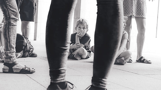 grayscale photo of children sitting on floor near people inside building during daytime thumbnail