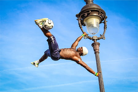 man wearing black shorts and pair of yellow sneakers holding on gray metal light post thumbnail