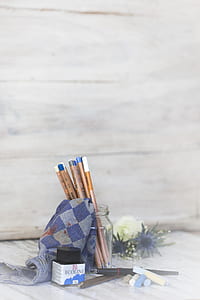 pencils in round clear glass jar beside blue and gray textile on white surface thumbnail