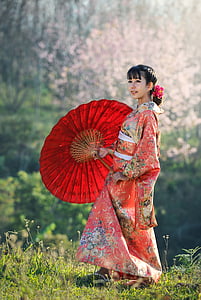 woman wears pink and multicolored floral dress holds red folding umbrella thumbnail