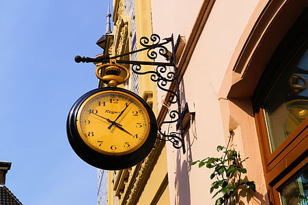 round black and beige analog clock hanging on black metal rack under blue sky displaying 4:06 thumbnail