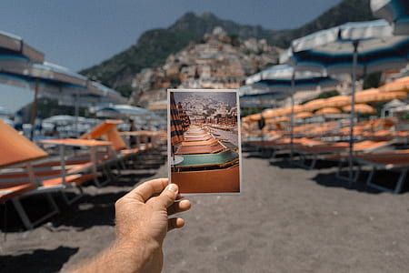 person holding photo of orange-and-gray beach patio umbrella and lounger chair lot during daytime thumbnail