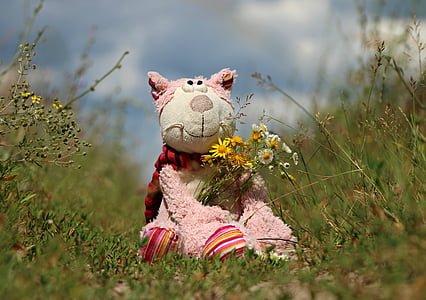 white and pink animal plush toy on holding flowers on green grass thumbnail