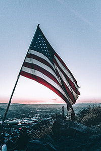 person sitting beside flag of United States of America near shore during daytime thumbnail