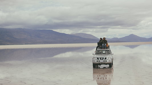 two people sitting top of silver Nissan vehicle traveling near mountain during daytime thumbnail