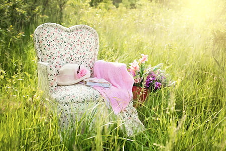 white, green, and pink floral fabric sofa chair with pink textile and hat on grass thumbnail