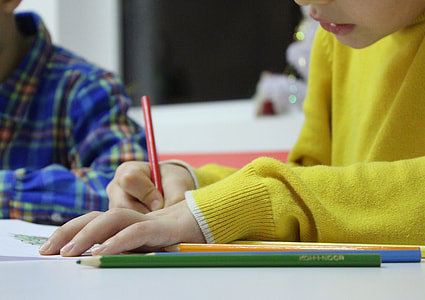 selective focus photography of person wearing yellow sweater while holding red pencil near white wooden table thumbnail