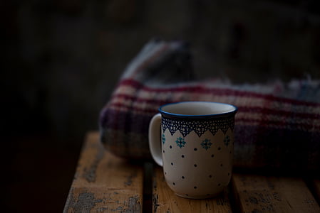 white and green ceramic mug on wooden table beside blanket thumbnail