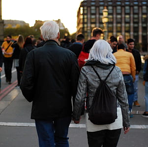 Man in Black Jacket Beside Woman in Grey Leather Jacket Holding Hands at Dusk in Busy Street thumbnail