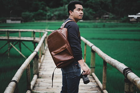 shallow focus photography of man carrying brown leather backpack standing on brown wooden platform during daytime thumbnail