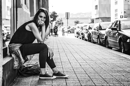 grayscale photography of woman wearing black top sitting on window rack thumbnail