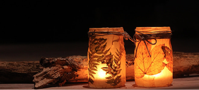 two candles in brown decorative jars beside firewood thumbnail
