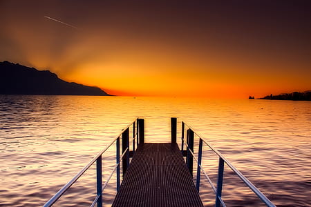 wooden dock on body of water with silhouette of mountains at distance thumbnail