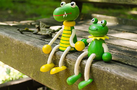 two green frog toys sitting on wooden bench during daytime thumbnail