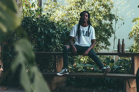 photo of man sitting on brown bench near two brown bottles thumbnail