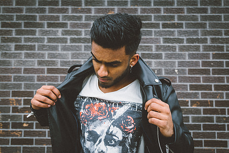 man holding his leather jacket beside concrete brick wall thumbnail