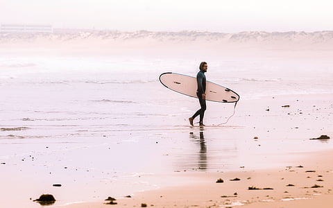 man walking on seashore while holding surfboard thumbnail