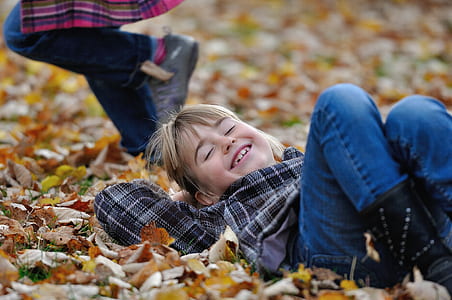 girl in black and brown plaid shirt with blue jeans lay on dried leaves thumbnail