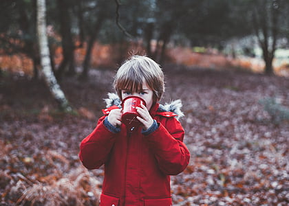 boy standing near trees while drinking on red cup thumbnail