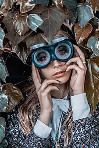 close-up photography of woman in long-sleeved top wearing goggles surrounded of leaves thumbnail