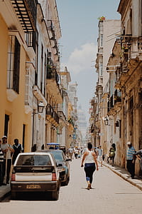 woman in white tank top and blue pants walking towards pathway between commercial building during daytime thumbnail