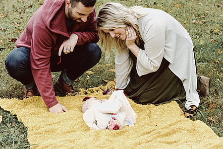 man and woman looking to the baby on grass with yellow blanket thumbnail