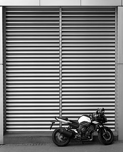 gray and black naked motorcycle beside gray roller shutter thumbnail