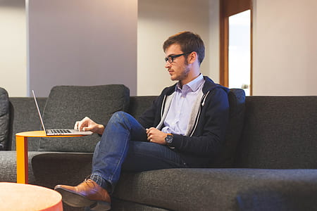 man in black zip-up jacket and blue denim jeans sitting on sofa thumbnail