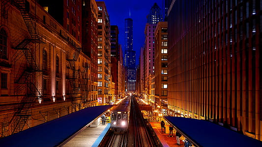 grey train with headlights on rail between buildings thumbnail
