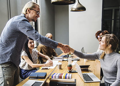 Man and Woman Shaking Hands in Middle of Brown Wooden Table thumbnail