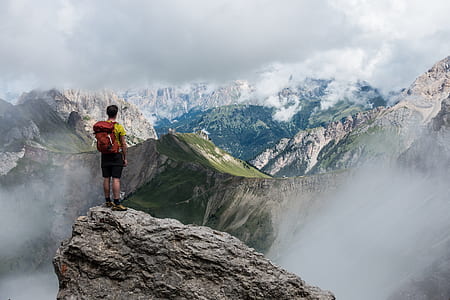 man in yellow shirt with red backpack standing on boulder looking over the mountains thumbnail