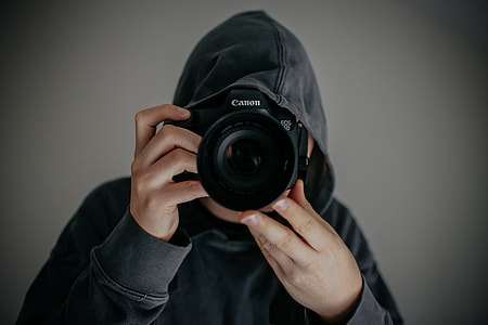 person wearing gray hoodie holding Canon DSLR camera thumbnail