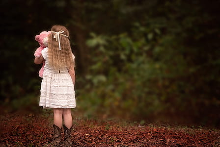 girl in white dress and pair of brown leather boots holding pink bear plush toy thumbnail