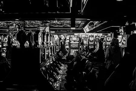 grayscale photography of man playing slot machine inside casino thumbnail
