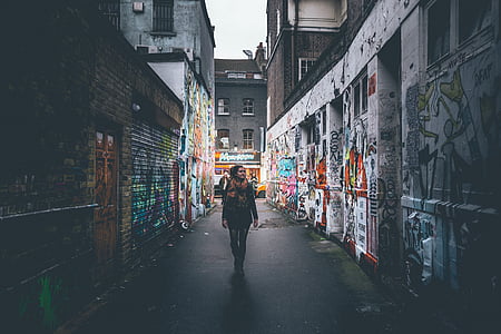 woman in black coat and pants walking between two building during daytime thumbnail