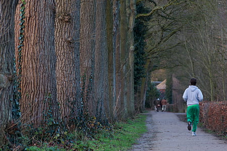 man wearing white hooded jacket and green pants near tree thumbnail