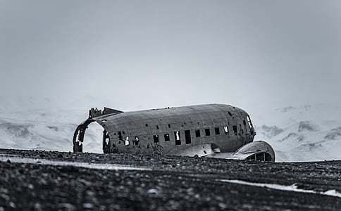 gray wrecked airplane on gravel ground overlooking snow covered mountain under white sky at daytime thumbnail