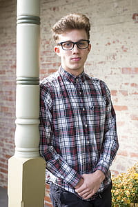 Man in Red Black and White Plaid-printed Dress Shirt Wearing Wayfarer Eyeglasses Leaning on White Wooden Post thumbnail