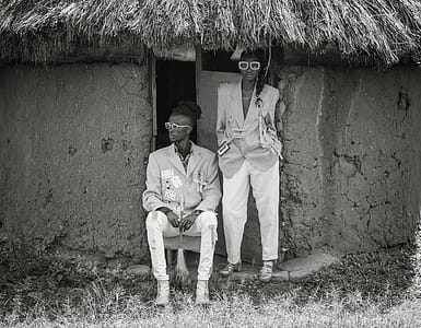 Grayscale Photo of Man and Woman Wearing Suit Beside Concrete House thumbnail