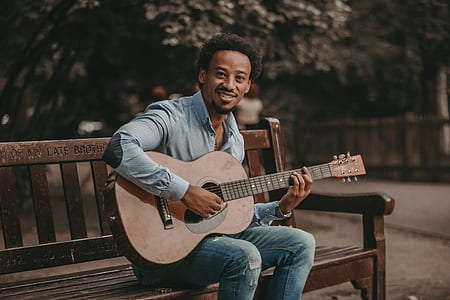 man sitting on park bench playing guitar thumbnail