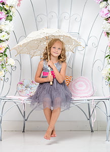 smiling girl in gray sleeveless dress sitting on white bench holding white umbrella thumbnail