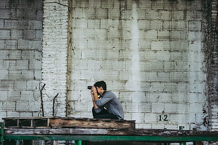 man using black camera beside gray wall thumbnail