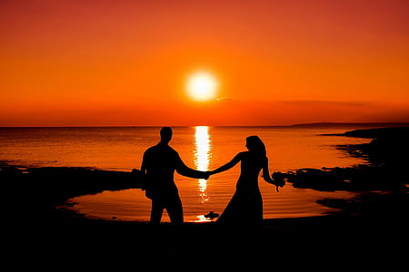 silhouette of man and woman holding hand stands near ocean at sunset thumbnail
