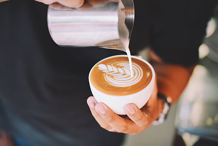 person making flower design on cup of cappuccino thumbnail