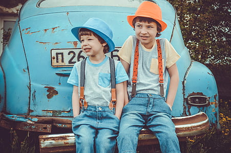 two toddlers sitting on blue Volkswagen Beetle coupe rear bumper during daytime thumbnail