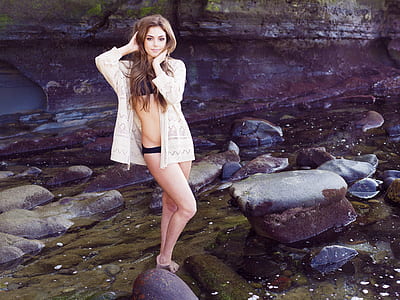 woman wearing bikini top and panties with cover up standing on body of water near rocks thumbnail