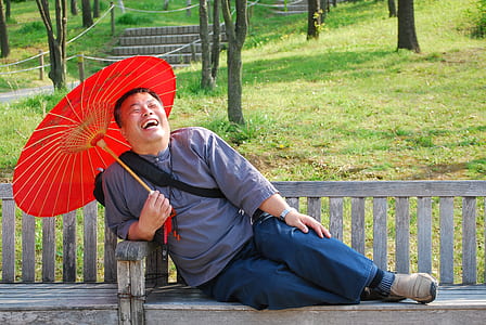 man laughing while sitting on bench holding oil paper umbrella thumbnail