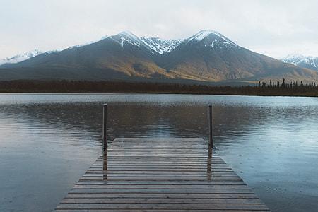 brown wooden dock on calm body of water in distance brown mountain under white sky at daytimke thumbnail