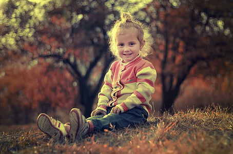 girl wearing pink and white cardigan and blue pants sitting on grasses thumbnail